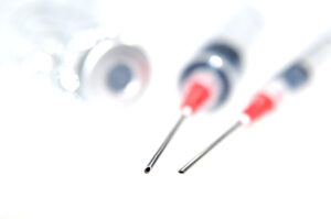 two syringes and a vial on white background - focus set on the needle tips